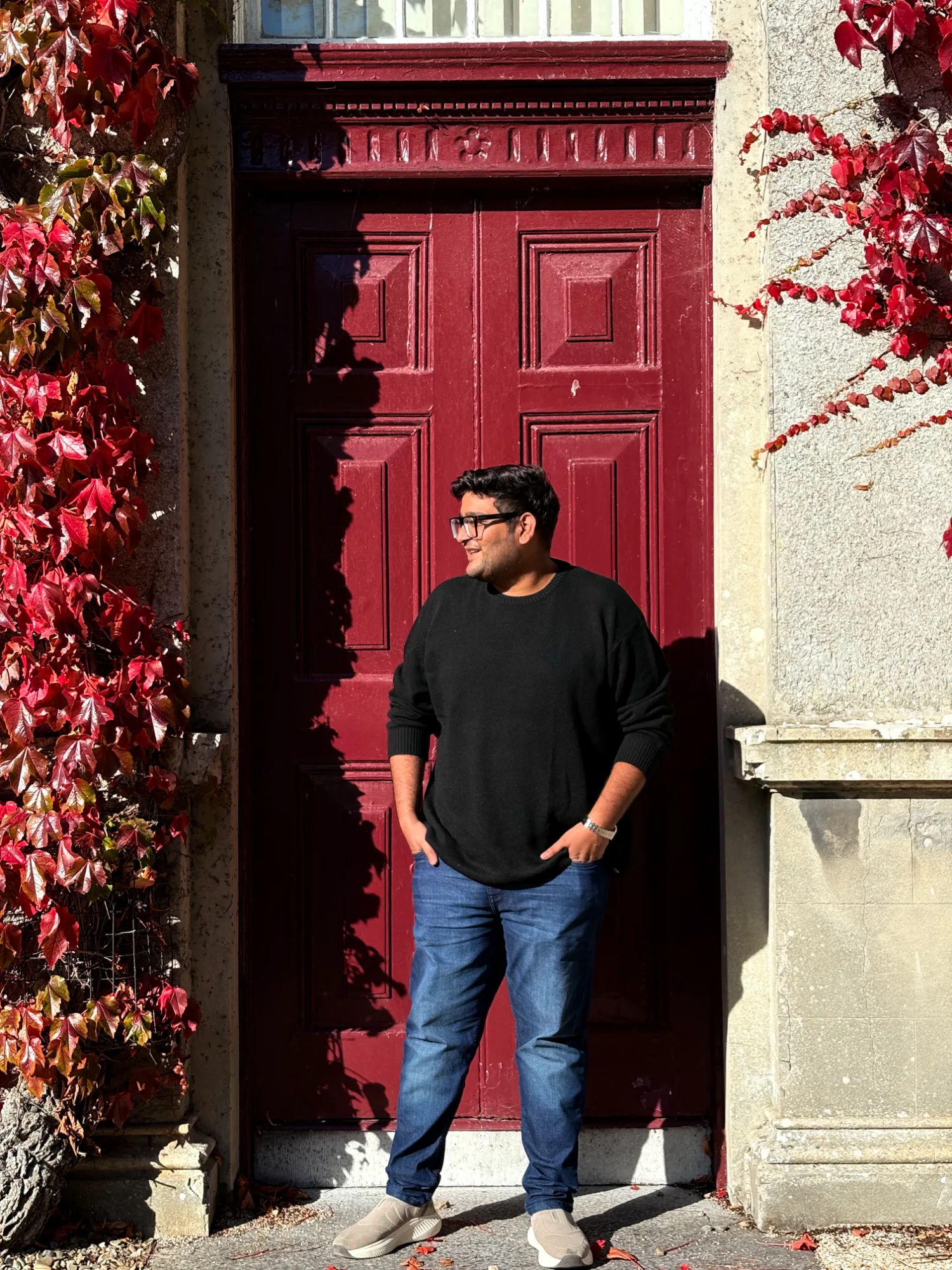Anirudh Chugh standing in front of a red door framed by autumn vines